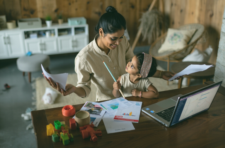 Happy Indian mom multitasking with her child on her lap, symbolizing the 'supermom' trap and the guilt around asking for help