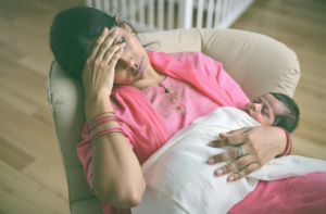 Indian mom with her baby, showing subtle signs of fatigue and emotional distress that capture the fine line between normal tiredness and postpartum depression